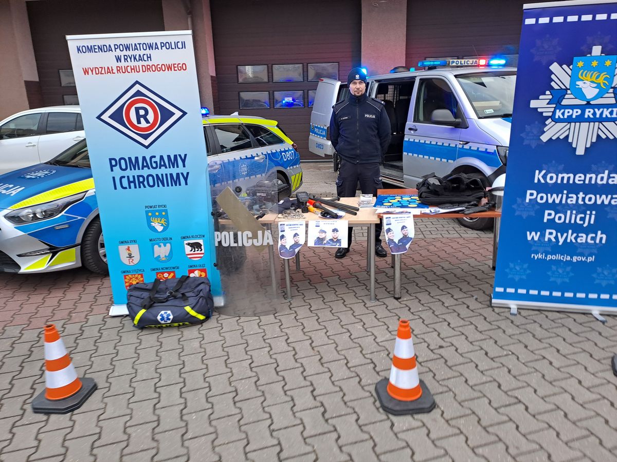 Stoisko Komendy Powiatowej Policji w Rykach na finale w WOSP w Rykach na placu OSP przy kinie Renesans. Widoczne pojazdy służbowe radiowozy oznakowane i nieoznakowane, osoby odwiedzające i sprzęt policyjny.