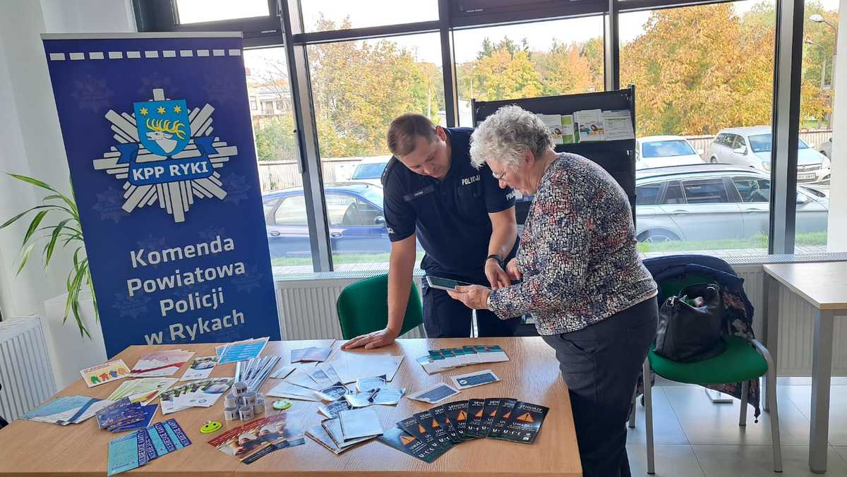 Stoisko Policji z Ryka w Zakładzie Ubezpieczeń Społecznych w Rykach na którym jest policjant oraz seniorka