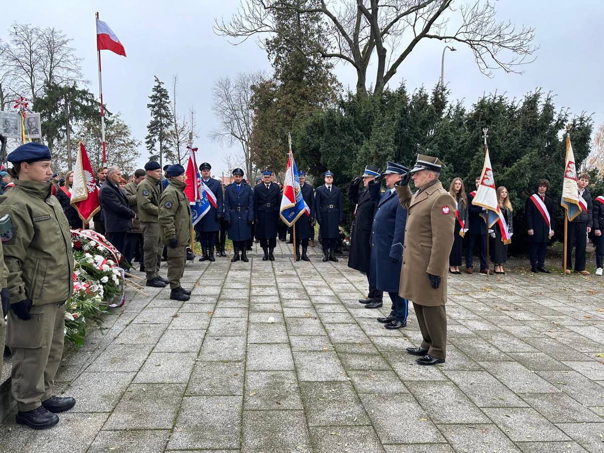 ""Powiatowe uroczystości w Rykach z okazji Narodowego Święta Niepodległości. Na miejscu widać zgromadzone osoby poczty sztandarowe oraz delegacje służb mundurowych składające wieniec.