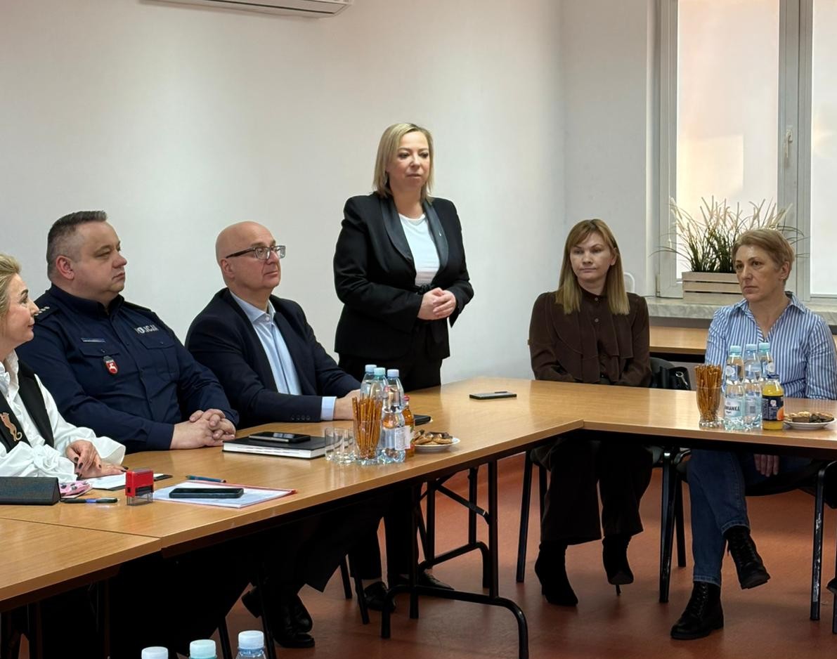 Uczestnicy konferencji siedzą przy stole jedna kobieta stoi i przemawia