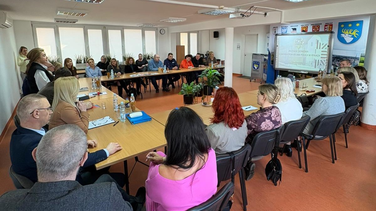 Uczestnicy konferencji siedzą przy stole jedna kobieta stoi i przemawia