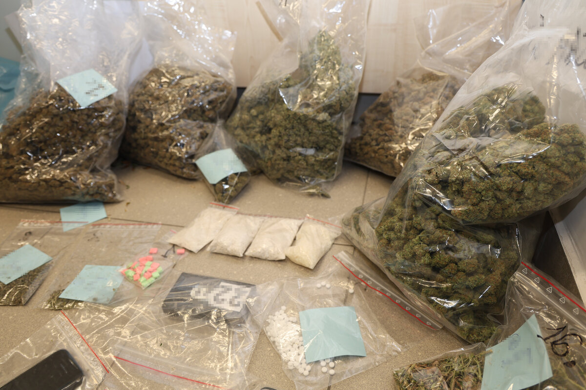 Zabezpieczone narkotyki różnego rodzaju w postaci suszu i tabletek w woreczka foliowych oraz zabezpieczone urządzenia jak telefon i waga ustawione na podłodze