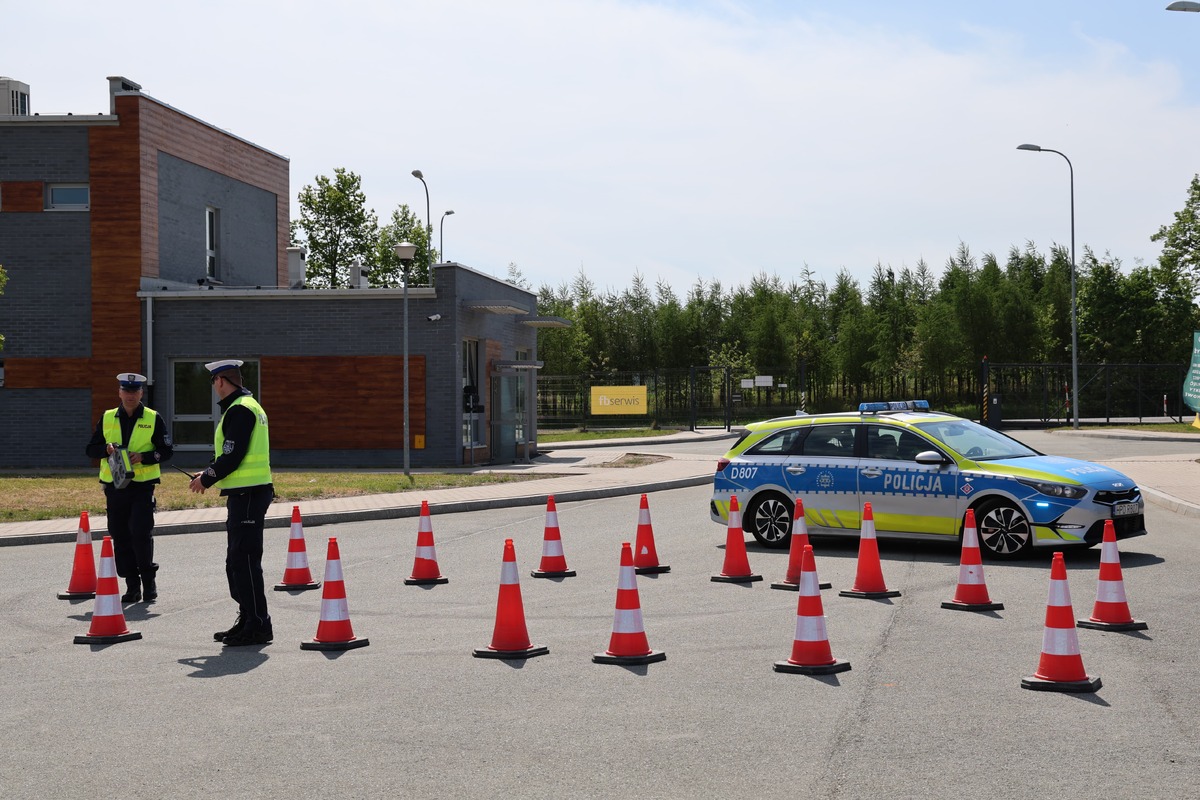 Radiowóz policyjny i policjanci stoją obok pachołków  zabezpieczają miejsce ćwiczeń