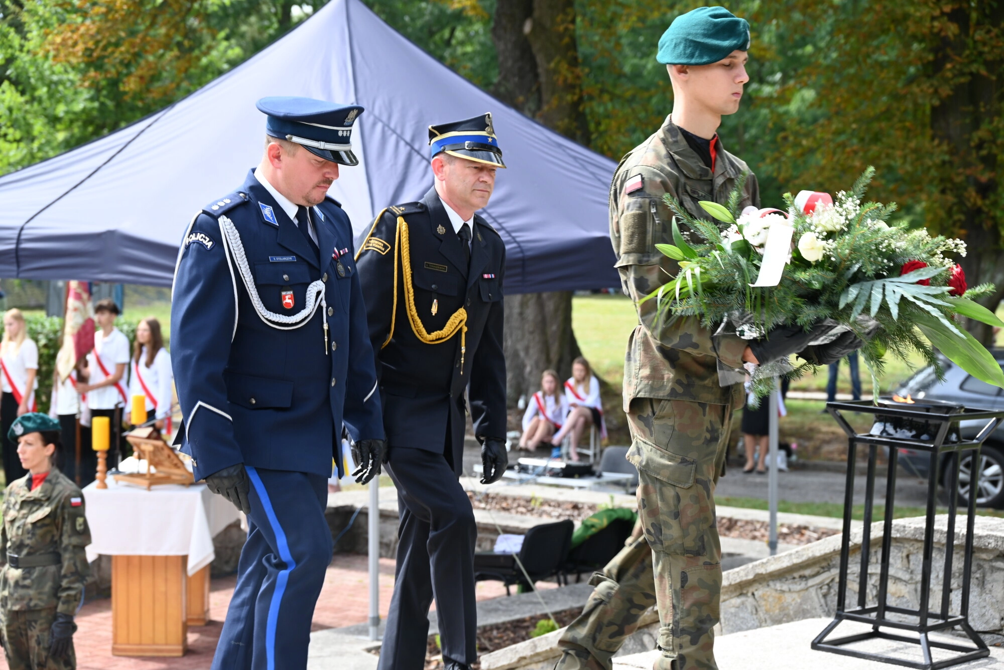 Funkcjonariusze policji i straży poznanej stoją przed pomnikiem i składają wieniec