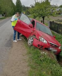 samochód marki Kia koloru czerwonego częściowo w przydrożnym rowie, a przy otwartych prawych drzwiach nieumundurowany policjant w kamizelce koloru żółtego