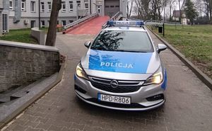 Radiowóz Policji oznakowany marki Opel koloru srebrnego z niebieskimi naklejkami