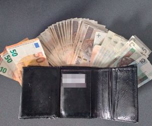 Na zdjęciu widoczny otwarty  portfel koloru czarnego z zawartością pieniędzy i dokumentów