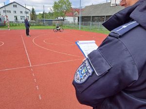 Na zdjęciu polisnat - jego ramię z naszywką policji ryckiej w tle zawodnik z rowerem podczas konkurencji sprawnościowej na boisku