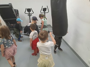 Zdjęcie przedstawia przedszkolaków zwiedzających siłownię. Oglądają sprzęt do ćwiczeń.