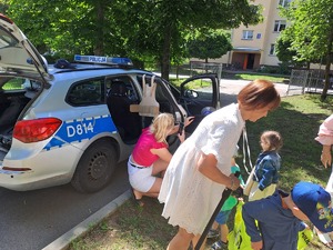 Na zdjęciu widoczna jest grupa przedszkolaków z nauczycielami podczas oglądania radiowozu policyjnego i wyposażenia policjanta