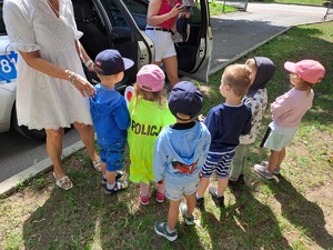 Na zdjęciu widoczna jest grupa przedszkolaków z nauczycielami podczas oglądania radiowozu policyjnego i wyposażenia policjanta