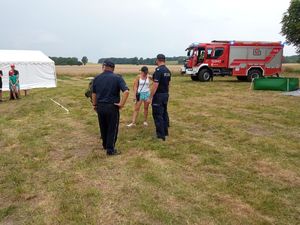 Zdjęcie przedstawia funkcjonariuszy policji umundurowanych, funkcjonariuszy straży pożarnej oraz uczestników obozu podczas ewakuacji zebranych na wykoszonym podłożu trawiastym w tle radiowozy policyjne oraz strażackie