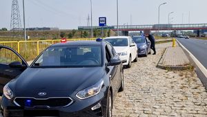 Jest to zdjęcie przedstawiające trzy samochody stojące na parkingu są to dwa nieoznakowane radiowozy oraz osobowa skoda koloru białego. przy jednym z pojazdów stoi osoba.