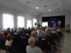 Zdjęcie przedstawia uczestników debaty społecznej zorganizowanej w Gminnym Ośrodku Kultury w Stężycy. Zaproszeni gości siedzą na krzesełkach prelegent policjant stoi .