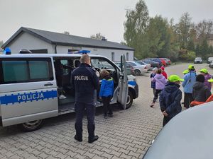 Zdjęcie przedstawia grupę dzieci ze szkoły podstawowej nr 2 w Dęblinie ubrane w różne kolorowe ubrania, Dzieci zwiedzają obiekt Komendy Powiatowej Policji w Rykach i zapoznają się ze sprzętem wykorzystywanym w słuzbie.