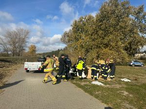 Na zdjęciu widoczna jest grupa strażaków oraz policjant którzy nasypują worki z pisakiem które ładują na przyczepkę podczepiona do quada