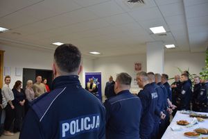 Uczestnicy spotkania opłatkowego policjanci, policjantki oraz pracownicy Komendy Powiatowej Policji w Rykach oraz ksiądz kapelan. Widoczny jest stół nakryty obrusem oraz dania wigilijne.