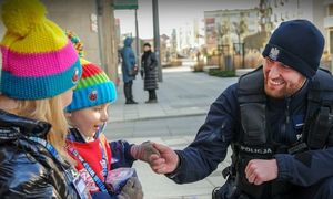 Umundurowany policjant przekazujący pieniądze kwestującym dzieciom wolontariuszom