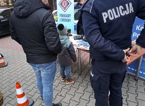 Stoisko Komendy Powiatowej Policji w Rykach na finale w WOSP w Rykach na placu OSP przy kinie Renesans. Widoczne pojazdy służbowe radiowozy oznakowane i nieoznakowane, osoby odwiedzające i sprzęt policyjny.