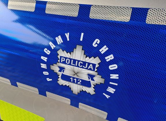 Naklej znajdująca się na radiowozie policji z logiem policji i napisem Pomagamy i chronimy. Naklejka jest koloru granatowego.