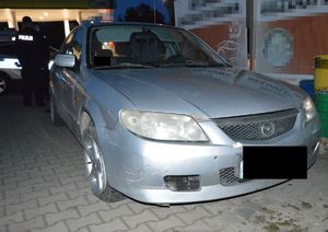 Samochód osobowy koloru srebrnego marki mazda zaparkowany na parkingu z widocznymi uszkodzeniami