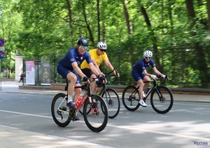 trzech mężczyzn w stroju sportowym kolarskim jadących na rowerach wyścigowych na ulicy w tle drzewa i zabudowania