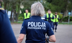 Policjanci w trakcie akcji poszukiwawczej. Na pierwszym planie odwrócona tyłem policjantka z napisem: Policja przewodnik psa