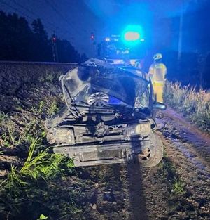 Uszkodzony samochód osobowym w wyniku zdarzenia w tle torowisko oraz wóz strażacki z włączonymi niebieskim światłem błyskowym