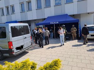 Zdjęcie stoiska policji ustawione przed budynkiem komendy policji w Rykach. Przy stoisku są odwiedzający oraz stoją pojazdy policyjne.