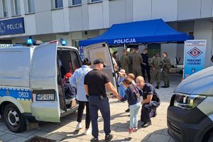 Zdjęcie stoiska policji ustawione przed budynkiem komendy policji w Rykach. Przy stoisku są odwiedzający oraz stoją pojazdy policyjne.