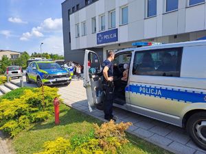 Radiowóz policyjny i odwiedzający gości oglądający go policjant prezentuje sprzęt.