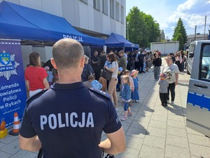 Zdjęcie stoiska policji ustawione przed budynkiem komendy policji w Rykach. Przy stoisku są odwiedzający oraz stoją pojazdy policyjne.