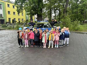 fotografia ze spotkani policjantów z przedszkolakami. Zdjęcie grupowe przedszkolaków z policjantami na tle radiowozu.