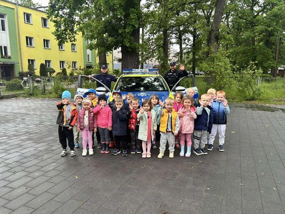 fotografia ze spotkani policjantów z przedszkolakami. Zdjęcie grupowe przedszkolaków z policjantami na tle radiowozu.