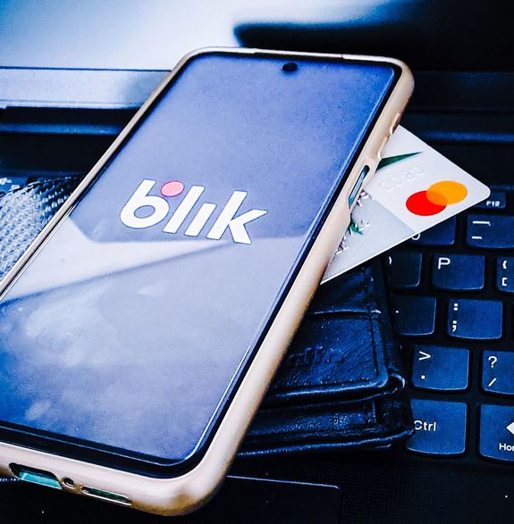 telefon komórkowy z napisem blik w po dni leża portfel koloru czarnego i kata płatnicza . Całość jest ułożona na klawiaturze laptopa.