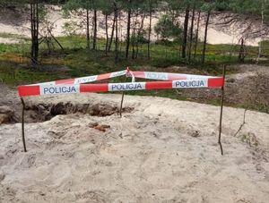 Niewybuchy z czasów II wojny Światowej leżące na piachu ogrodzone taśmą z napisem Policja.