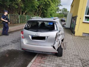 Pojazd toyota koloru srebrnego z uszkodzonym tyłem w tle radiowóz i policjant