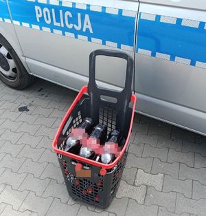 Koszyk sklepowy z napojami gazowanymi typu cola w tle radiowóz policji
