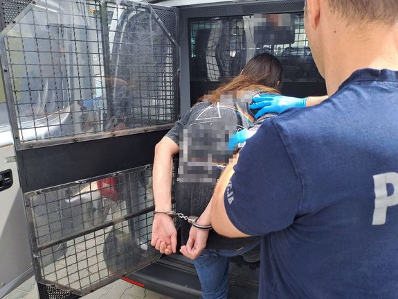 Osoba zatrzymana mężczyzna kajdankami wsiada do radiowozu prowadzona przez policjanta