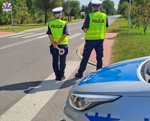 Policjanci kontrolują prędkość na drodze pstojąc obok radiowozu policji