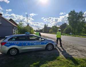 Policjanci podczas kontroli drogowej obok stoi radiowóz policji oznakowany