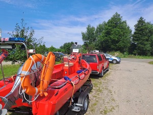Policjanci przygotowujący się do działań poszukiwawczych za zaginionym. widoczne są radiowozy policji zaparkowane na parkingu.