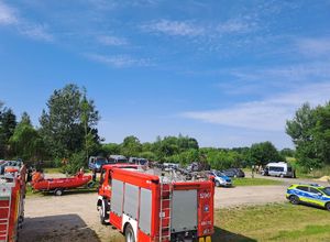 Policjanci przygotowujący się do działań poszukiwawczych za zaginionym. widoczne są radiowozy policji zaparkowane na parkingu.