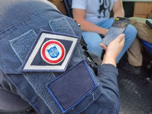 Policjanci przygotowujący się do działań poszukiwawczych za zaginionym. widoczne są radiowozy policji zaparkowane na parkingu.