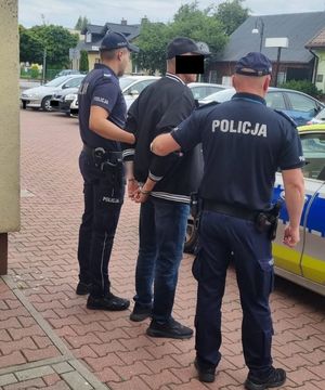 Zatrzymany z kajdankami na rękach prowadzony przez dwóch umundurowanych policjantów