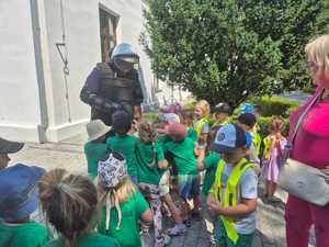 Policjant w ochraniaczach przeciwuderzeniowym prezentuje sprzęt  grupie dzieci