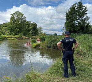 akcja poszukiwawcza na rzece Wieprz policjant obserwuje brzeg rzeki na wodzie pływają łodzie strażackie