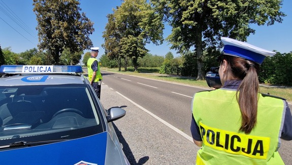 policjanta umundurowana dokonuje pomiaru prędkości obok stoi radiowóz w tle jest droga