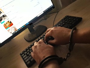 osoba siedząca pry biurku z kajdankami na rękach w tle monitor i klawiatura komputera