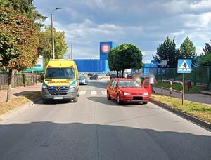 miejsce zdarzenia drogowego na drodze stoi ambulans oraz volkswagen koloru czerwonego w tle zabudowa miejska oraz pojazdy